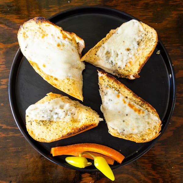 Four slices of cheesy garlic bread with peppers on a black plate from The Sub Station.
