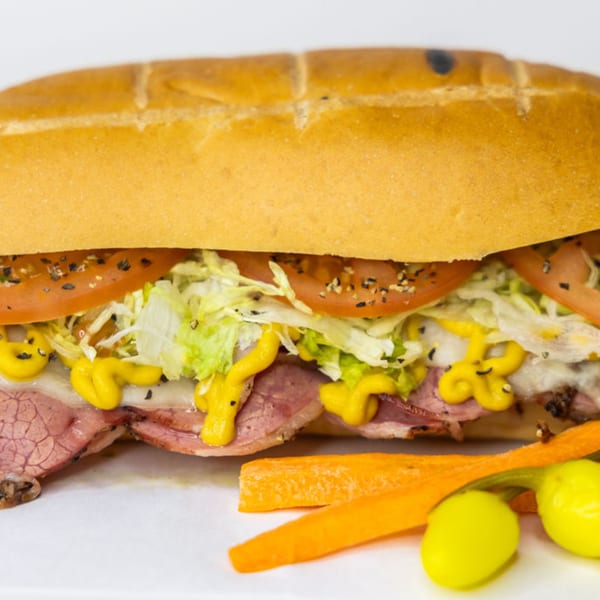 A Sub Station sandwich with meat, cheese, lettuce, tomatoes, and mustard, served with carrots and peppers.