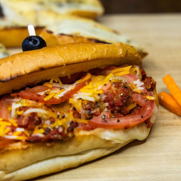 A Sub Station sandwich filled with meat, cheese, tomatoes, and onions, garnished with an olive.