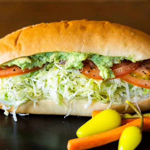 A Sub Station sandwich with guacamole, tomatoes, and shredded lettuce, with peppers and carrots.