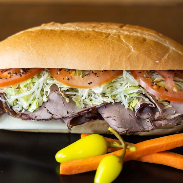 A Sub Station roast beef sub with lettuce, tomato, and peppers on a dark surface.