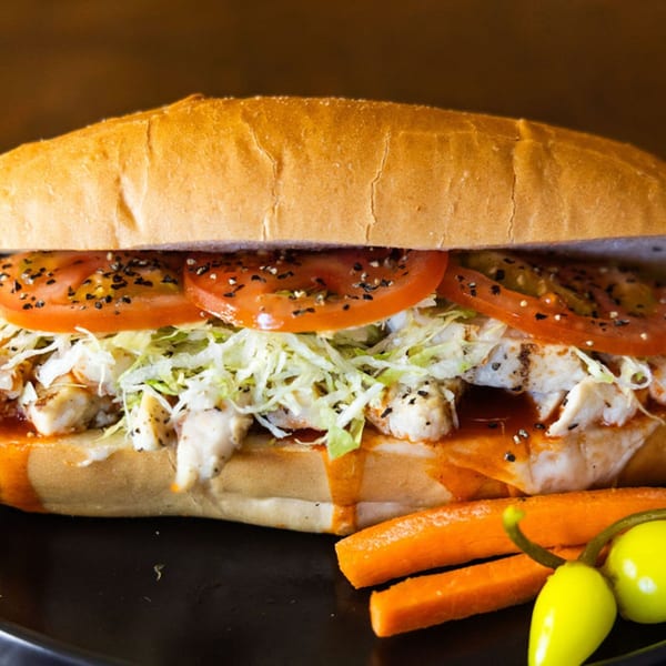 A Sub Station chicken sub with tomatoes, lettuce, and sauce, served with carrots and peppers.