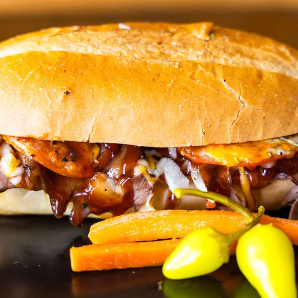 A Sub Station sandwich filled with meat, cheese, onions, and sauce, served with carrots and peppers.