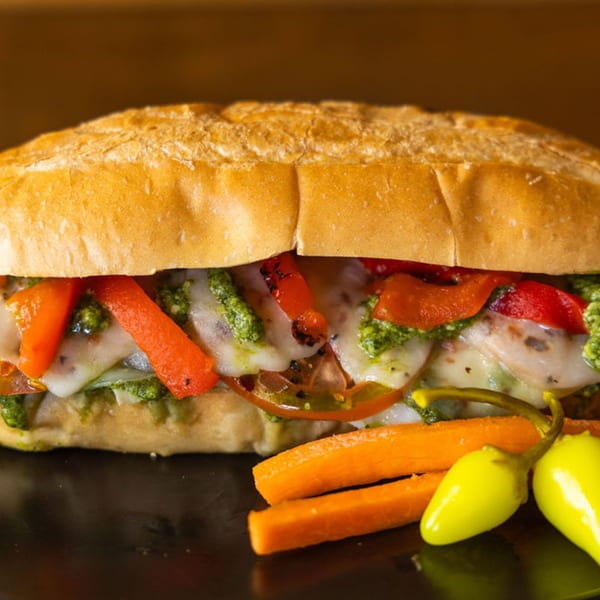 A Sub Station sandwich filled with melted cheese, red peppers, pesto, and tomatoes, served with carrots and peppers.