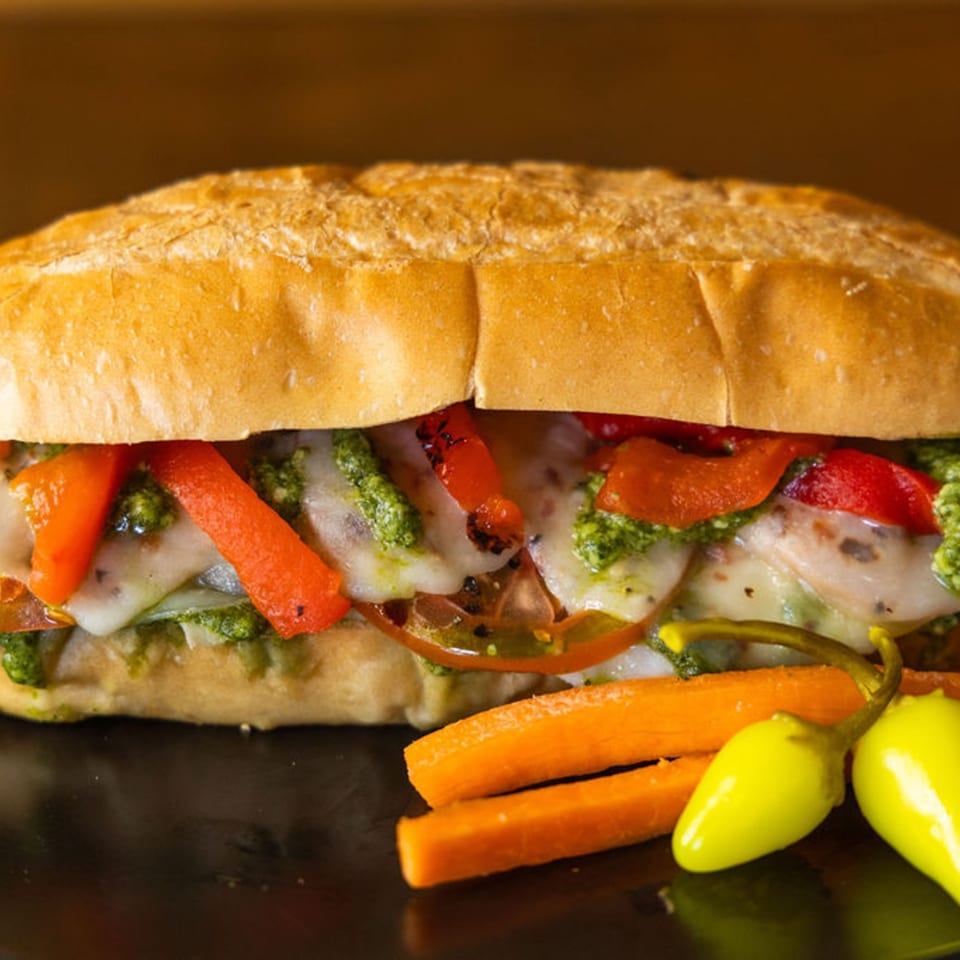 A Sub Station sandwich filled with melted cheese, red peppers, pesto, and tomatoes, served with carrots and peppers.