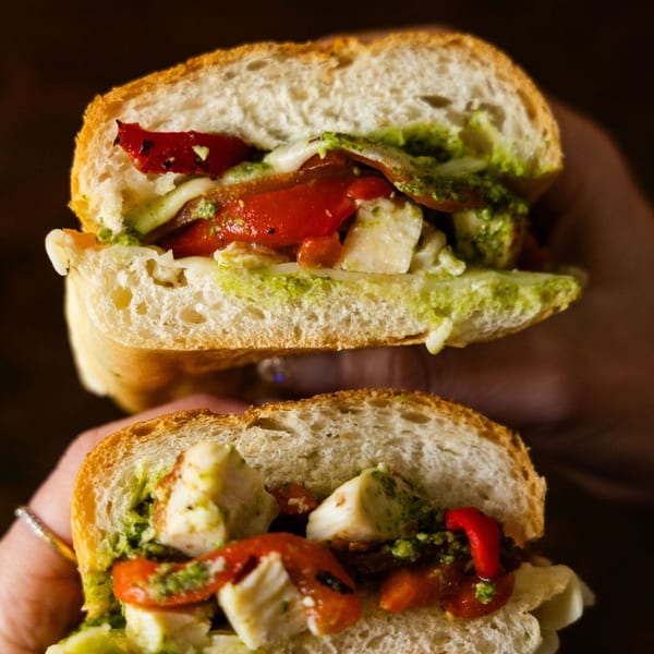 Two hands holding a Sub Station sandwich filled with mozzarella, roasted red peppers, and pesto.