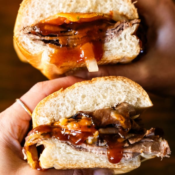 Two hands holding a Sub Station sandwich filled with meat, cheese, and sauce.