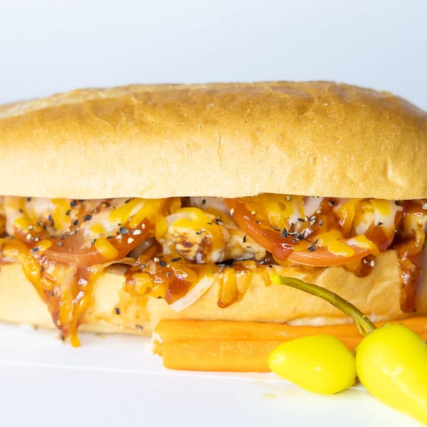 A Sub Station sandwich with melted cheese, tomatoes, onions, sauce, and black sesame seeds, with peppers and carrots.