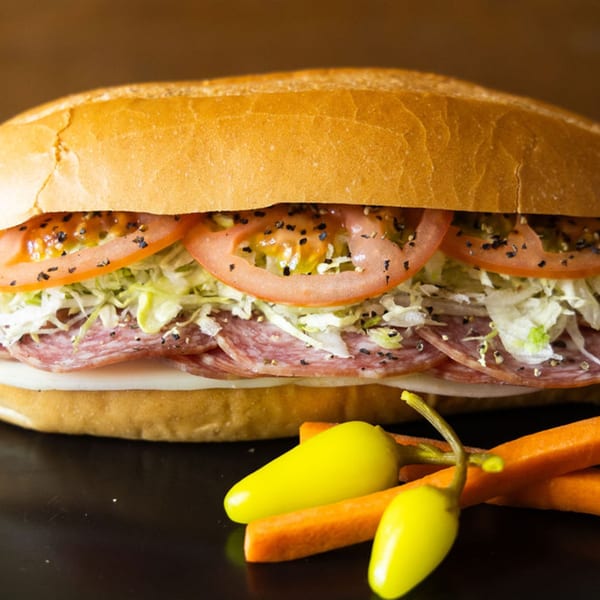 A Sub Station sandwich with salami, cheese, lettuce, and tomatoes, served with pickled peppers and carrots.