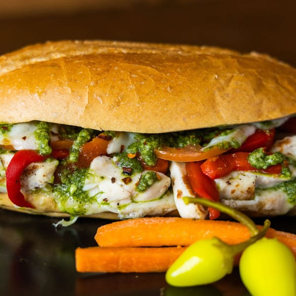 A Sub Station sandwich filled with chicken, red peppers, pesto, and melted cheese, with carrots and peppers.